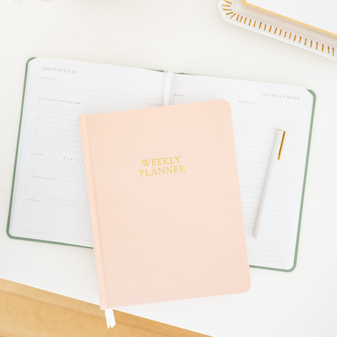 Open undated planner on desk with a pink weekly planner on top
