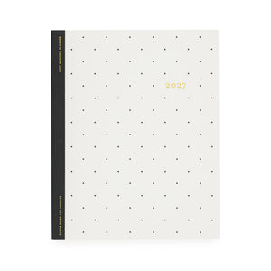 A minimalist 2027 monthly planner with a cream-colored cover decorated with a grid of small black dots and gold foil text with '2027' with a black tape binding