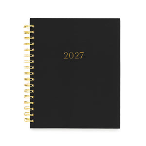 A black 2027 spiral-bound planner with gold lettering and gold wire binding with gold foil '2027' numbers