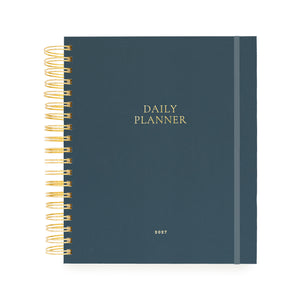 A navy blue daily planner with gold wire binding on the left and gold foil text reading 'DAILY PLANNER' and '2027' on the front cover