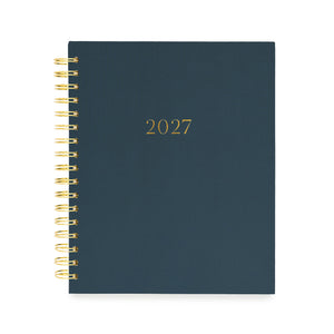 A 2027 spiral-bound planner with a dark navy blue cover and gold foil lettering