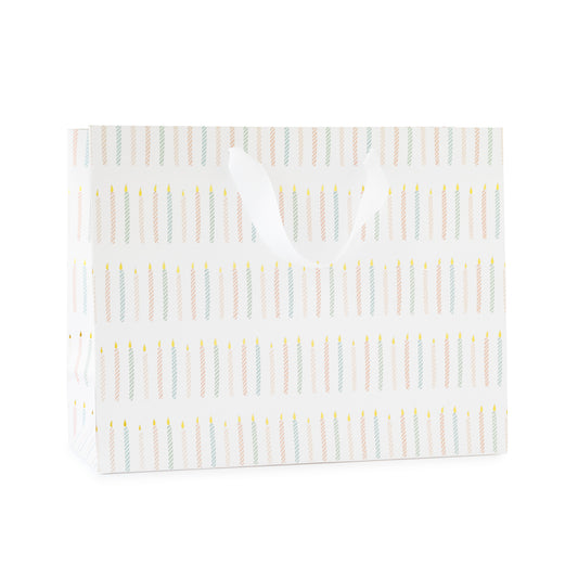 large gift bag with white ribbon handles printed with a colorful candle pattern in pink and blue with gold foil