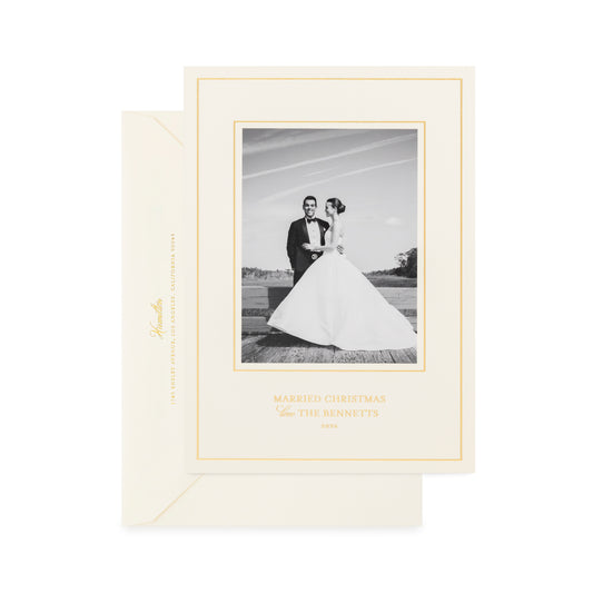An elegant cream-colored wedding Christmas greeting card with a gold border and champagne gold script text printed with 'married christmas love the bennetts' with a cream envelope