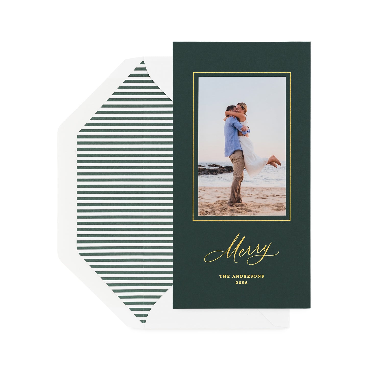 A vertical holiday card on racing green paper with gold foil details, shown with a white envelope featuring dark green horizontal striped liner.