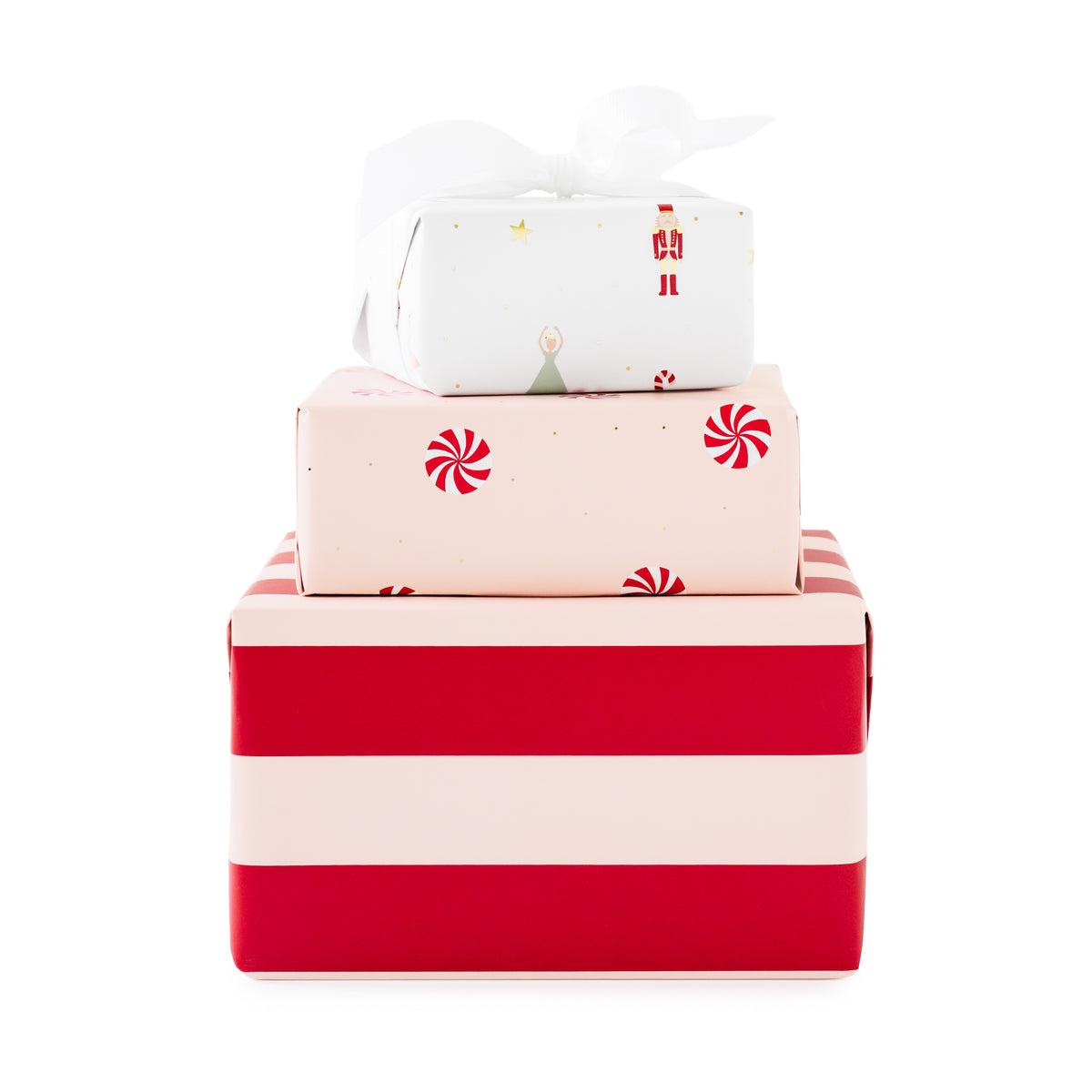 Three stacked gift boxes wrapped in festive holiday paper, with a white box with nutcracker icons and gold foil on top tied with a white ribbon, a light pink box in the middle with red candy cane icons, and a larger red and pale pink striped box at the bottom.