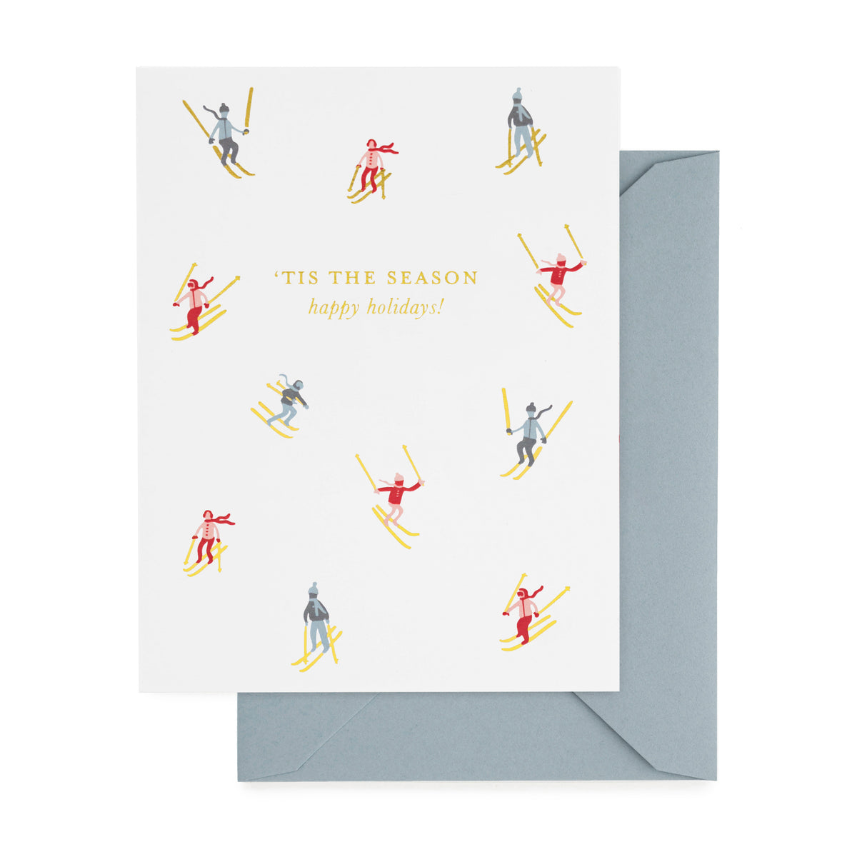 A white greeting card with the text 'TIS THE SEASON happy holidays!' and small illustrated skiers in red, blue, and gold foil, shown with a light blue envelope