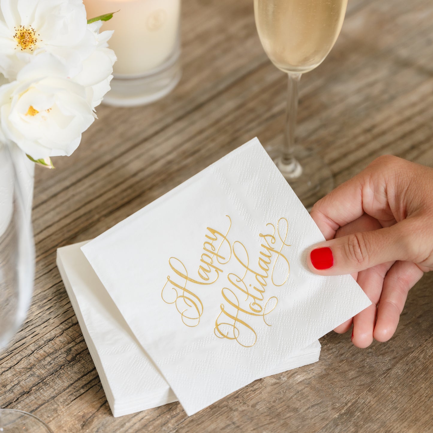 Gold happy holidays script napkins in hand with champagne flute