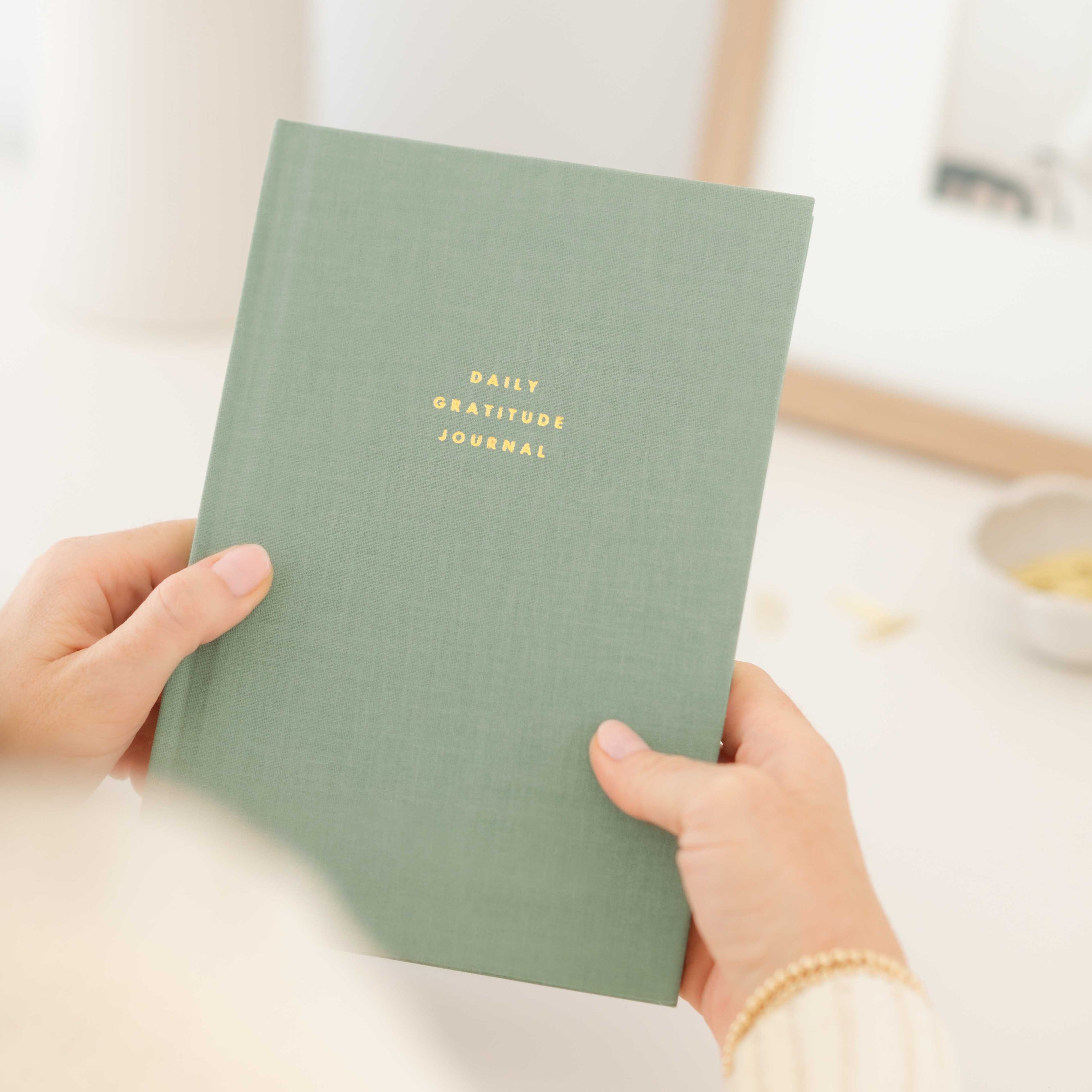 Green 'Daily Gratitude Journal' held by hands with a blurred background