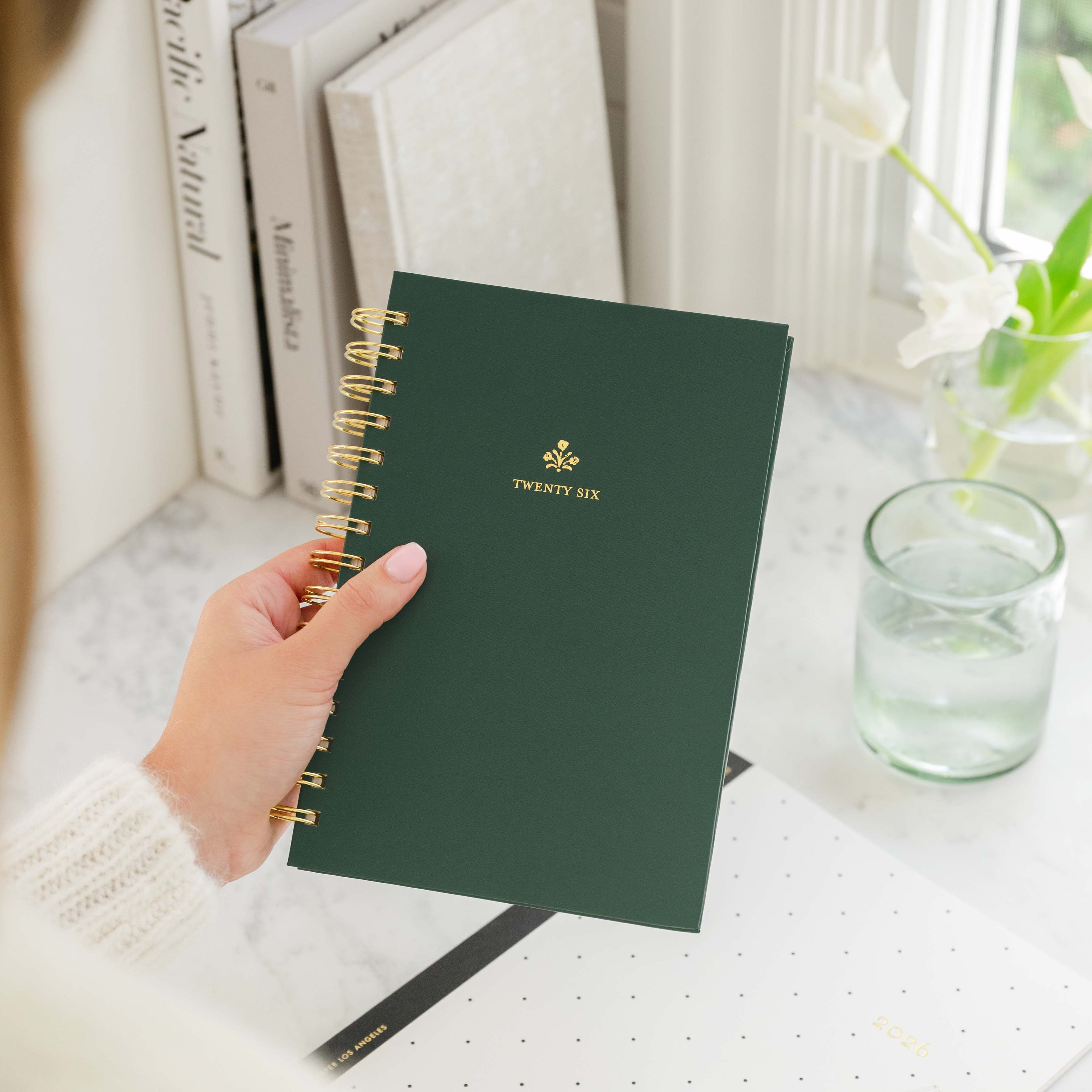 Hand holding a green planner with 'TWENTY SIX' on the cover