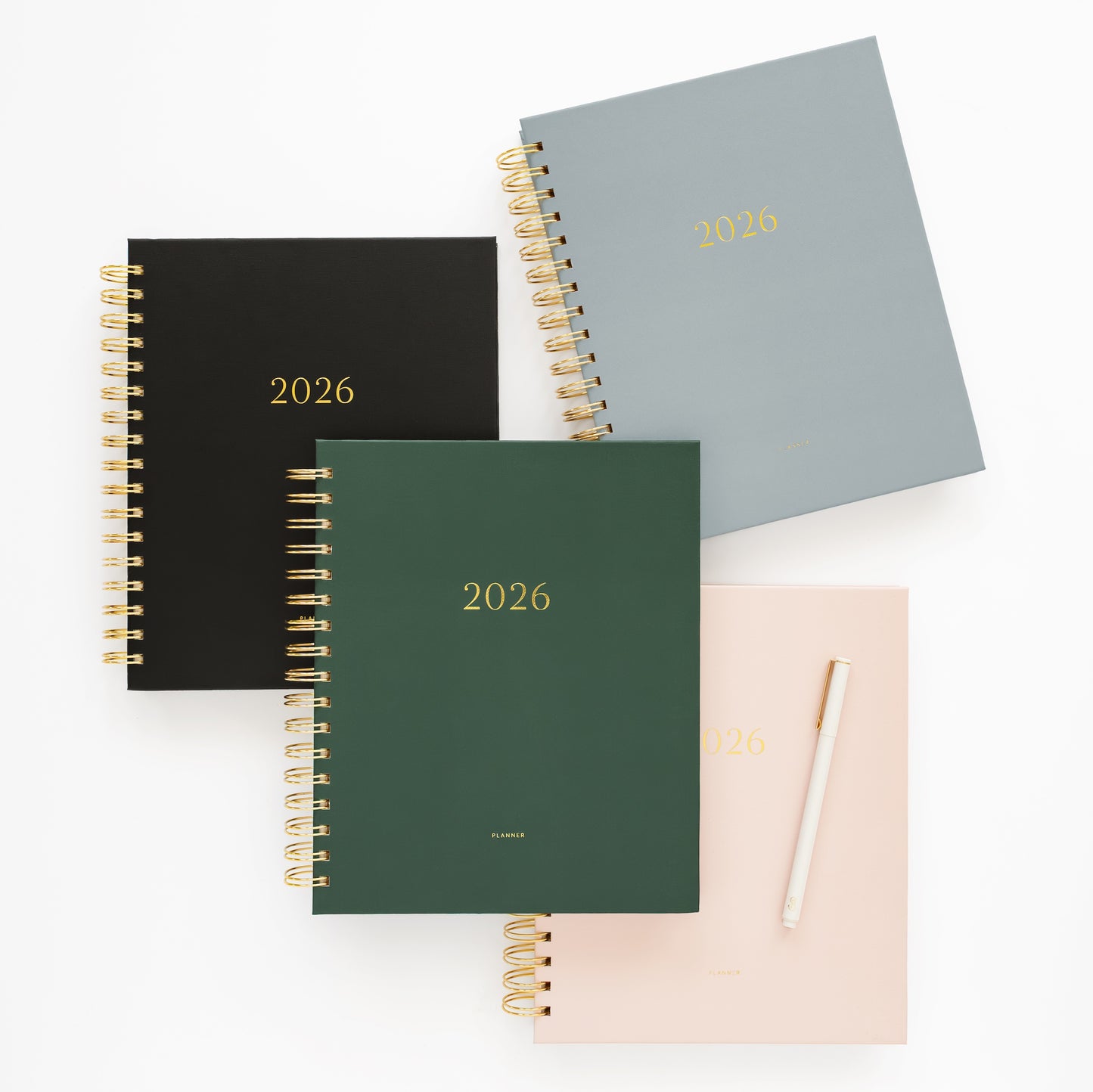 Four spiral-bound planners in black, green, and dusty blue with '2026' printed on them.