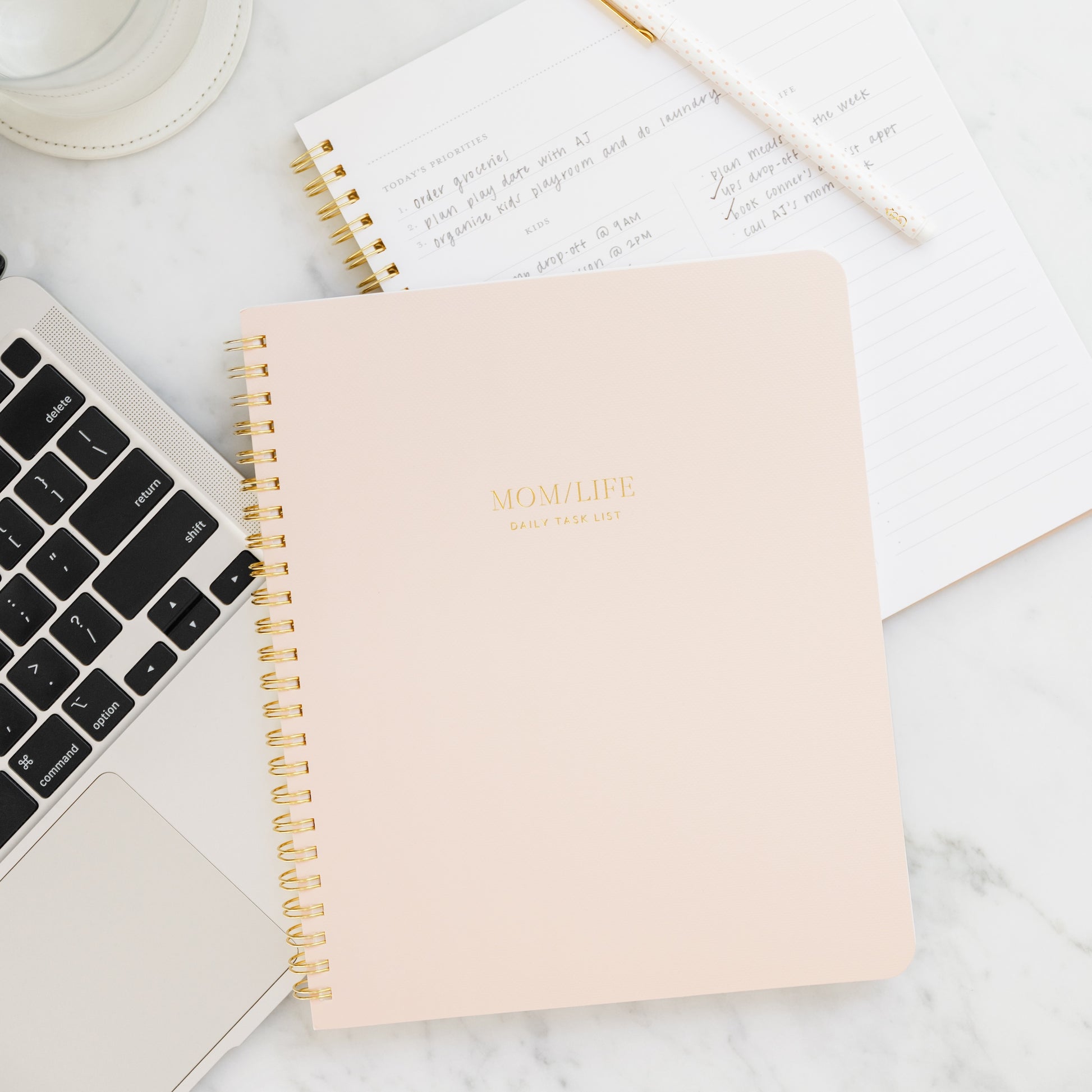 Pink spiral notebook with gold spiral binding and mom/life daily task list in gold foil on the cover