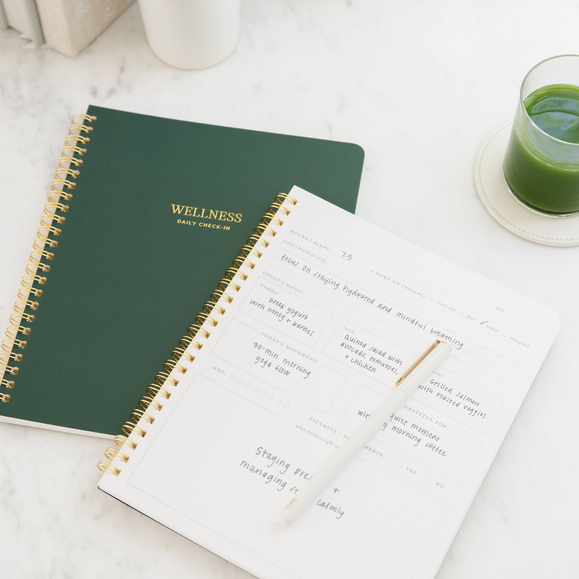 Open spiral-bound green notebook titled 'Wellness' on a light surface with a glass of green juice.
