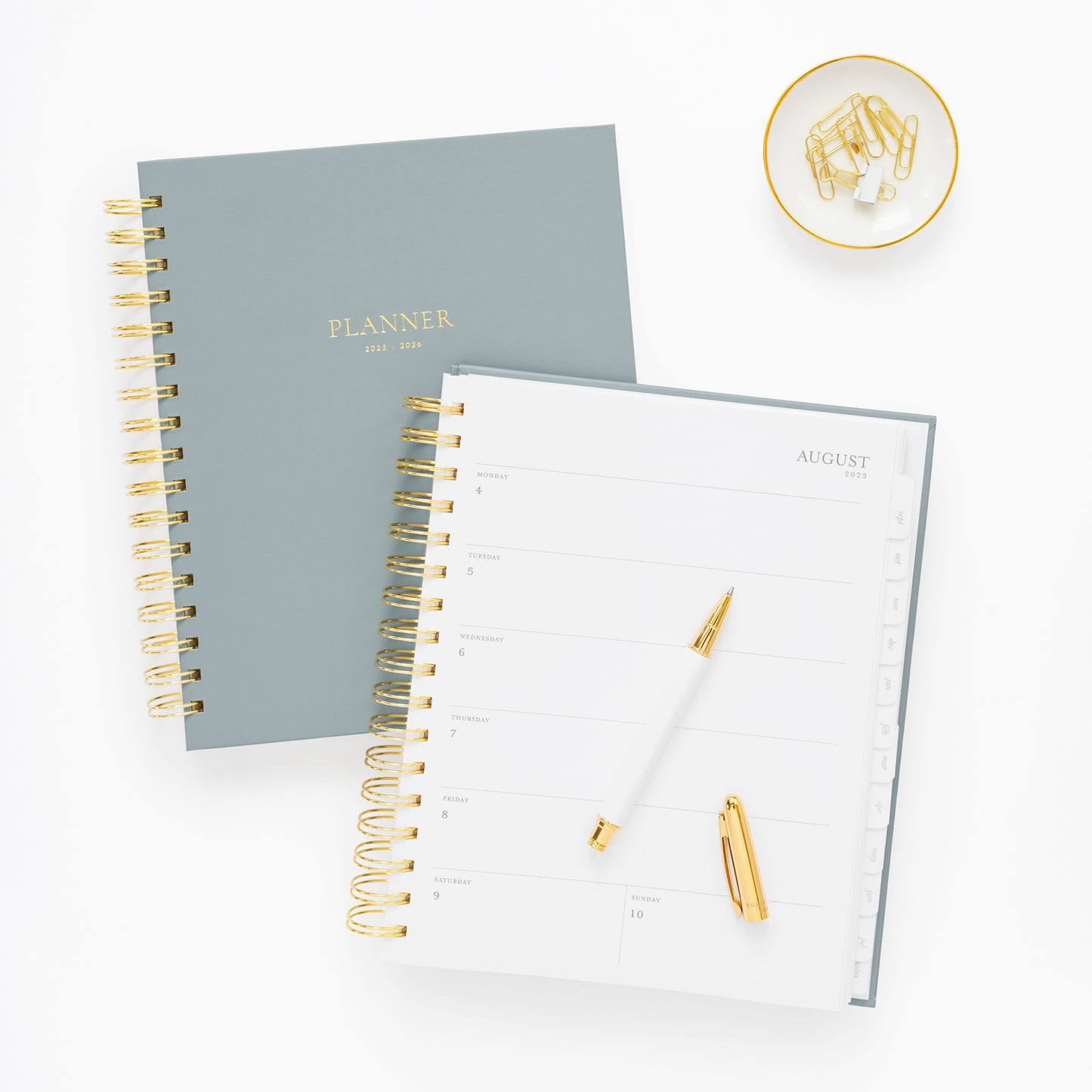 dusty blue spiral planner 1 closed and 1 open to a weekly page, with pen and paper clips