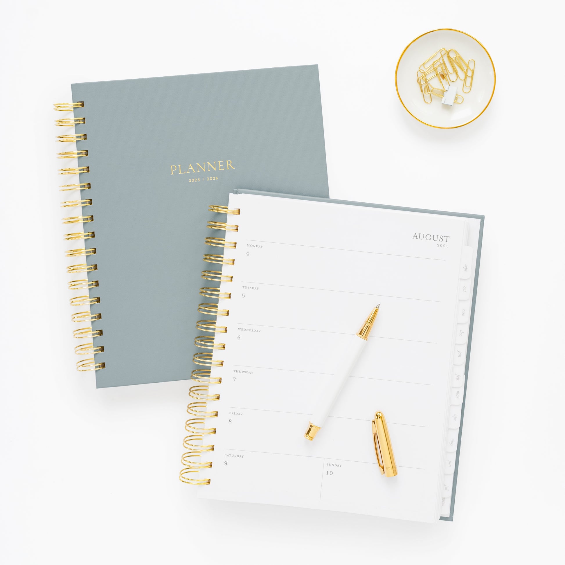 dusty blue spiral planner 1 closed and 1 open to a weekly page, with pen and paper clips