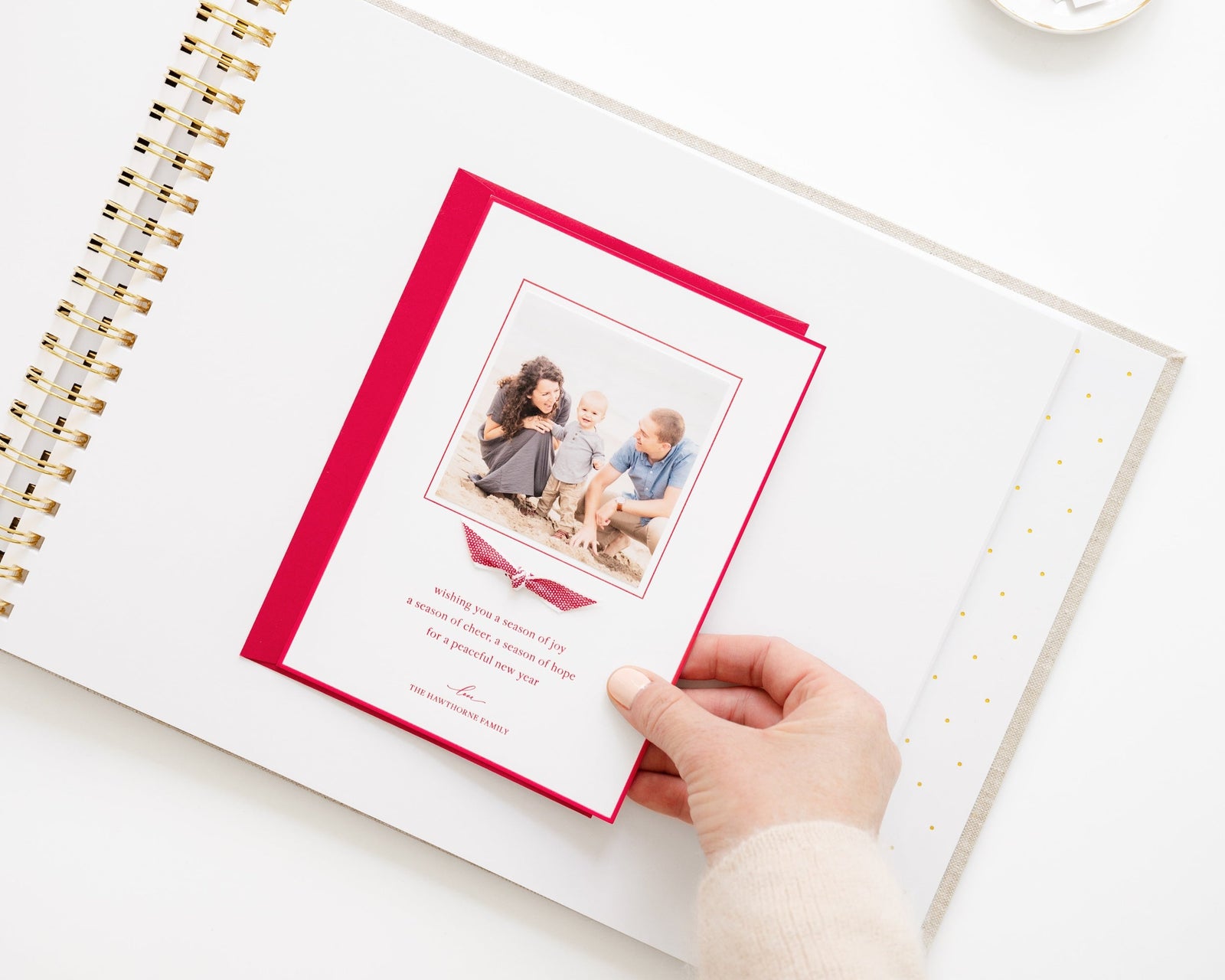 holiday card book open with a red and white holiday family photo card being pasted onto the page