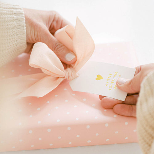 Rose and white dot wrapped gift with woman adding gift tag to package