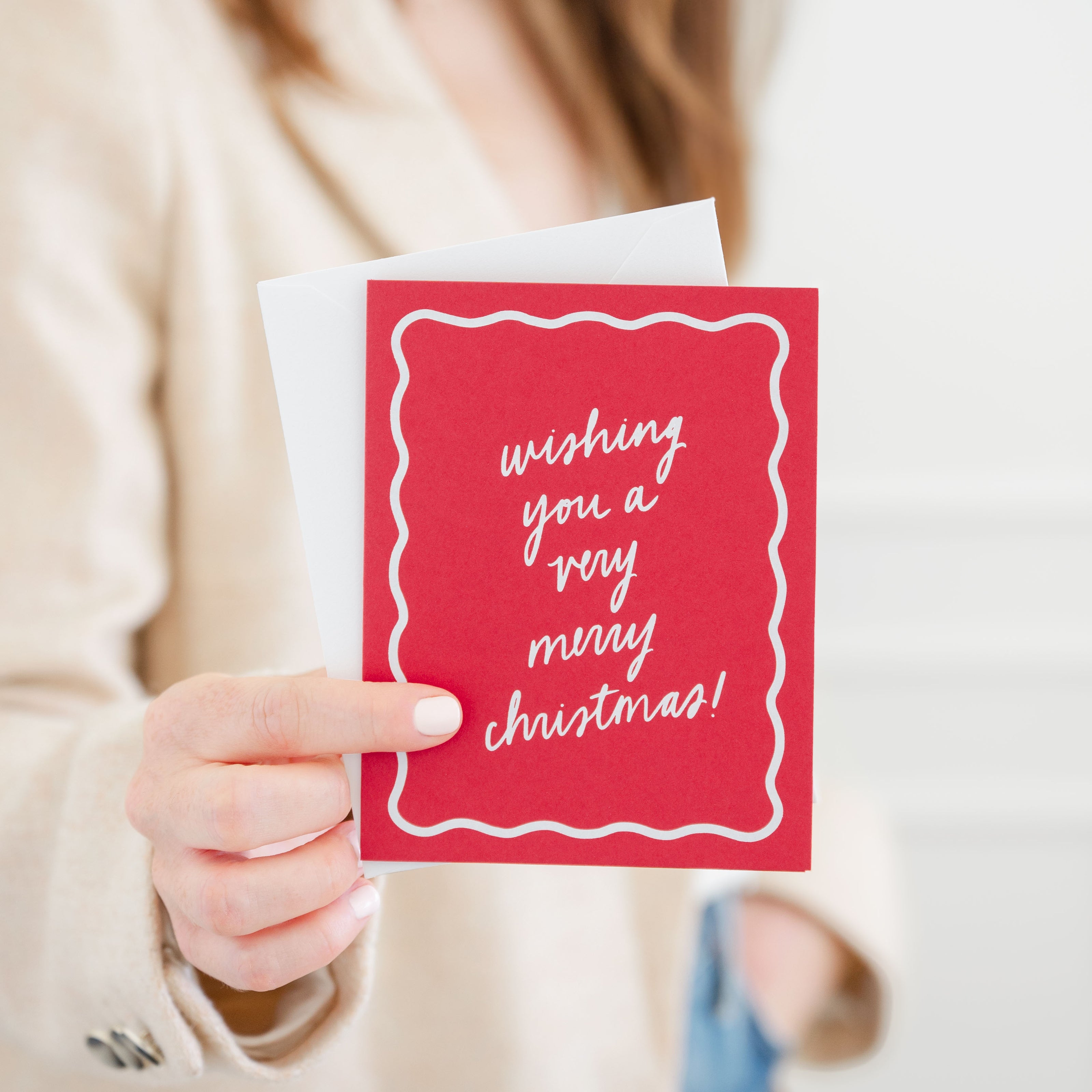 Person holding a red Christmas card with 'wishing you a very merry christmas' paired with a white envelope