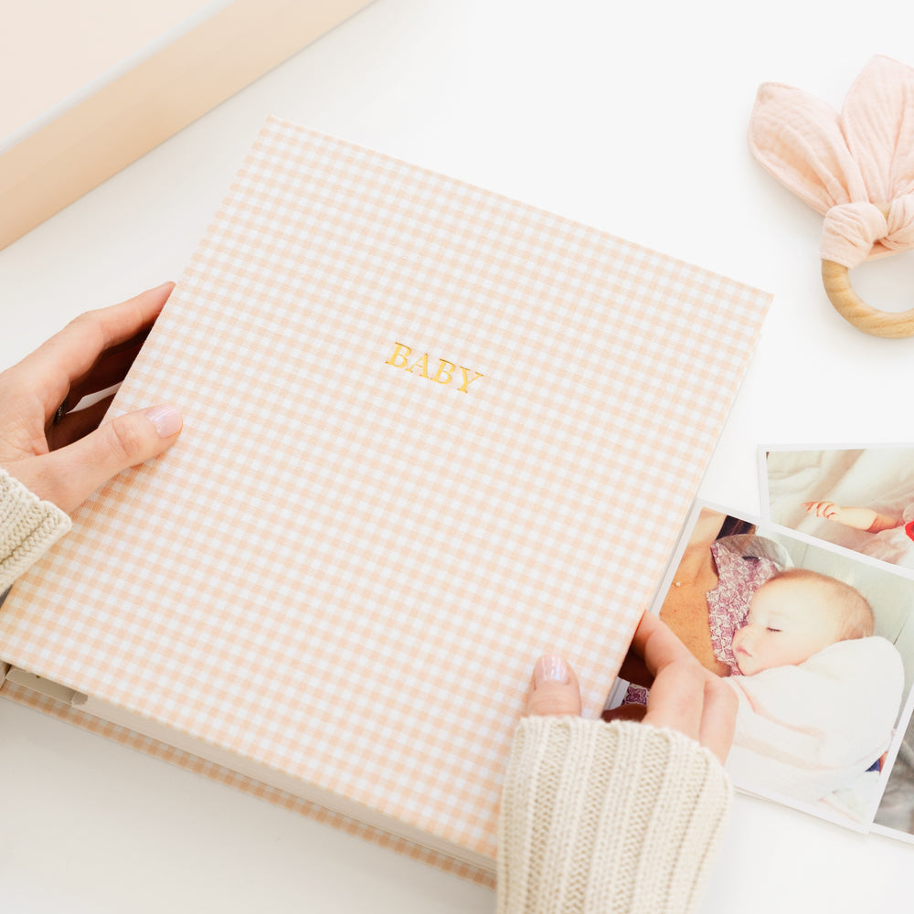 pink gingham baby book on a desk with photos