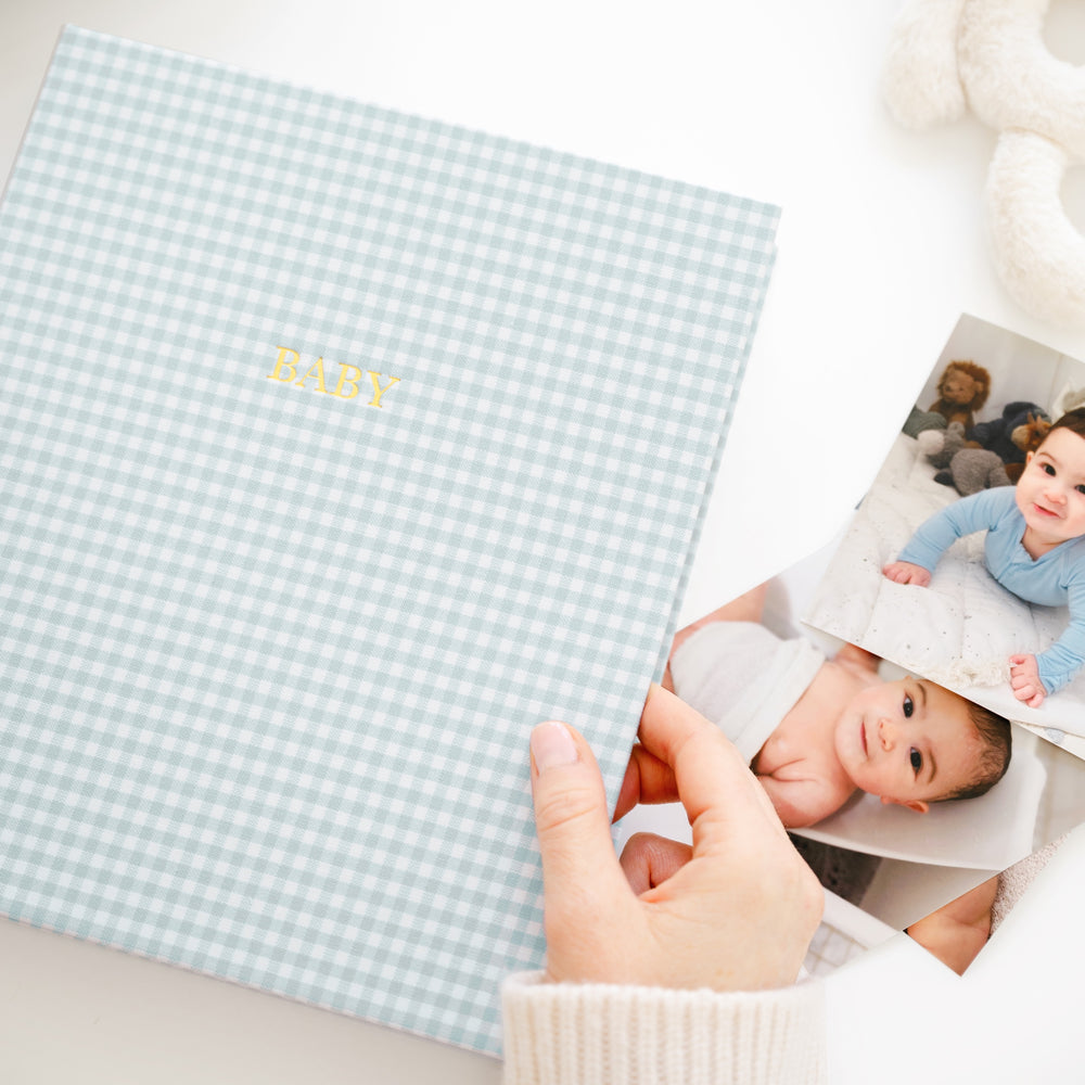 blue gingham baby book on a desk with photos
