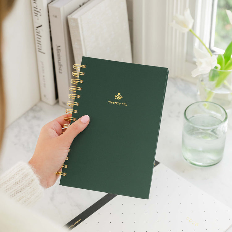 Green small spiral planner in hands with 'twenty six' in gold foil on cover