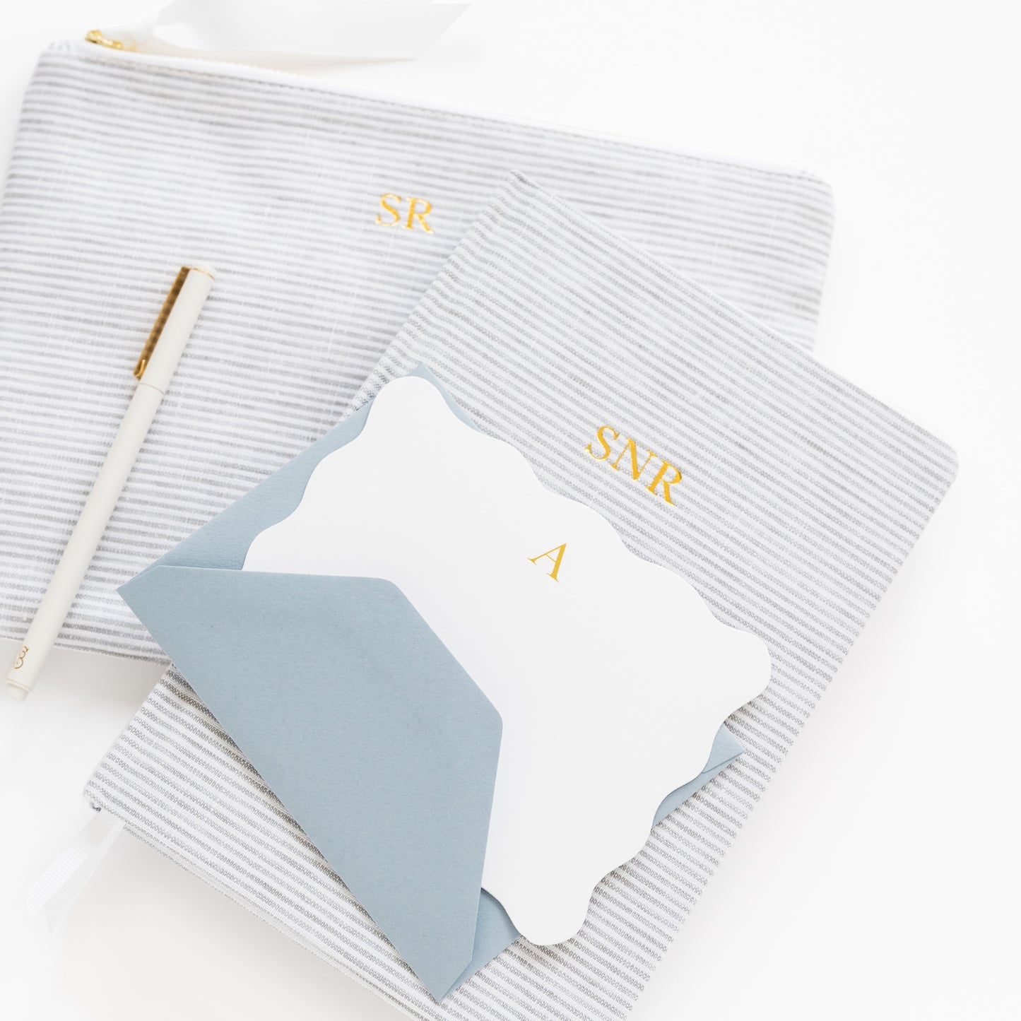 Grey striped fabric journal with 'SNR' initials and grey striped pouch with 'SR' initials with a white scalloped card and blue envelope with 'a' in gold foil