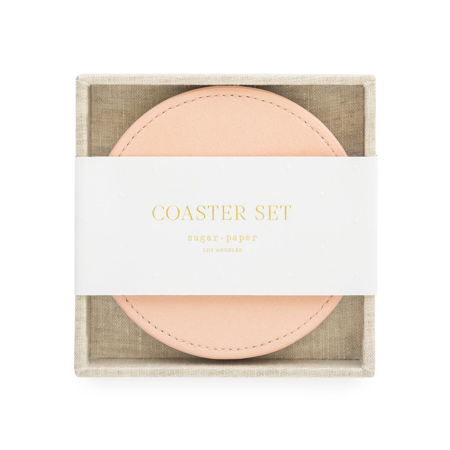A set of pink vegan leather coasters with a fabric tray holder, packaged for sale with 'coaster set' and sugar paper logo printed on a white belly band in gold foil