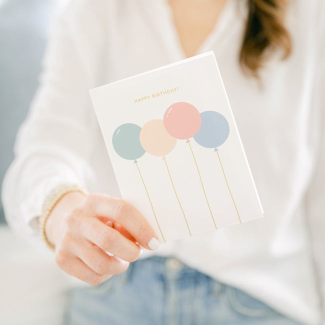 Woman holding a card with colored birthday balloons