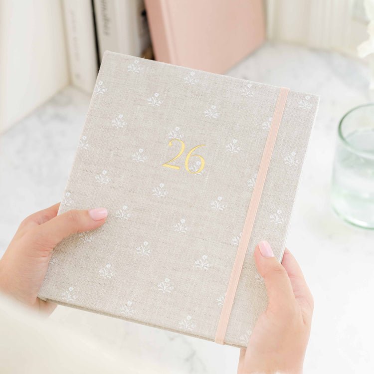 Person holding a fabric planner with '26' on the cover in gold foil