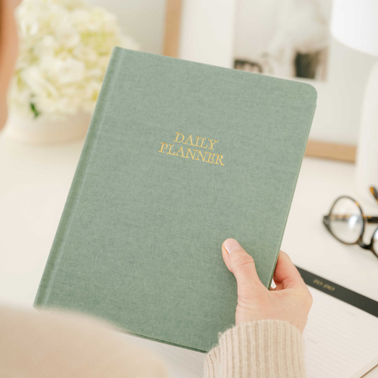 Green daily planner held by a hand at a desk setting