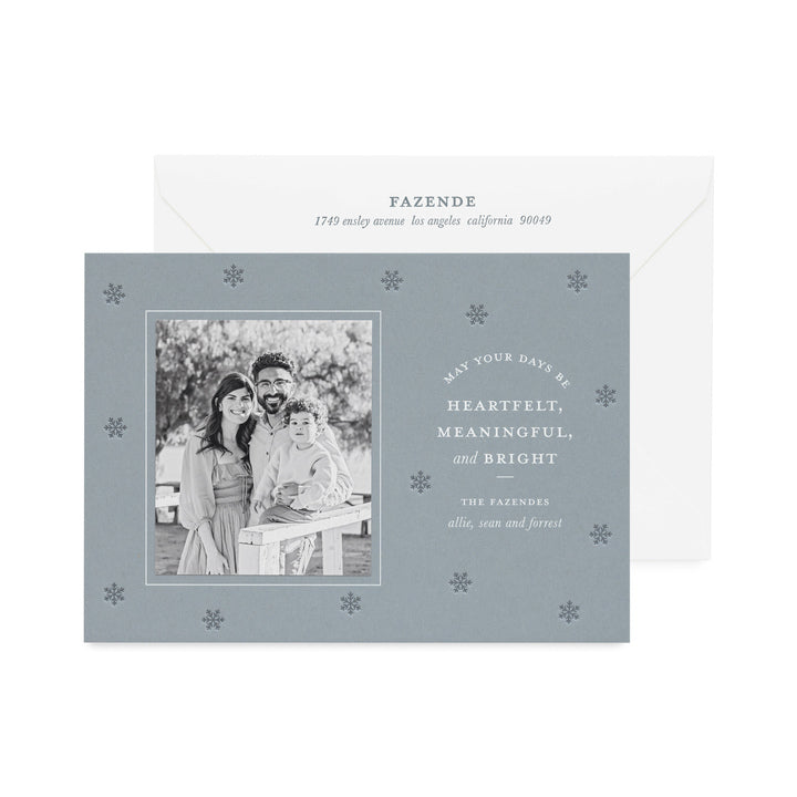 Coastal blue custom holiday photo card paired with a black and white photo with white foil greeting 'may your days be heartfelt, meaningful, and bright' with dark blue snowflake pattern letterpress printed paired with a white envelope with dark blue return address