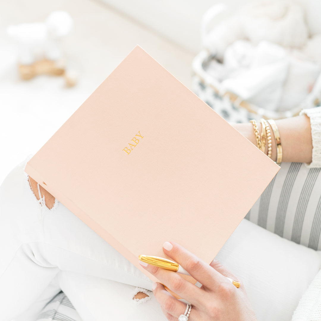 This shows the detail of the baby book with gold foil "baby" and pale pink fabric cover.