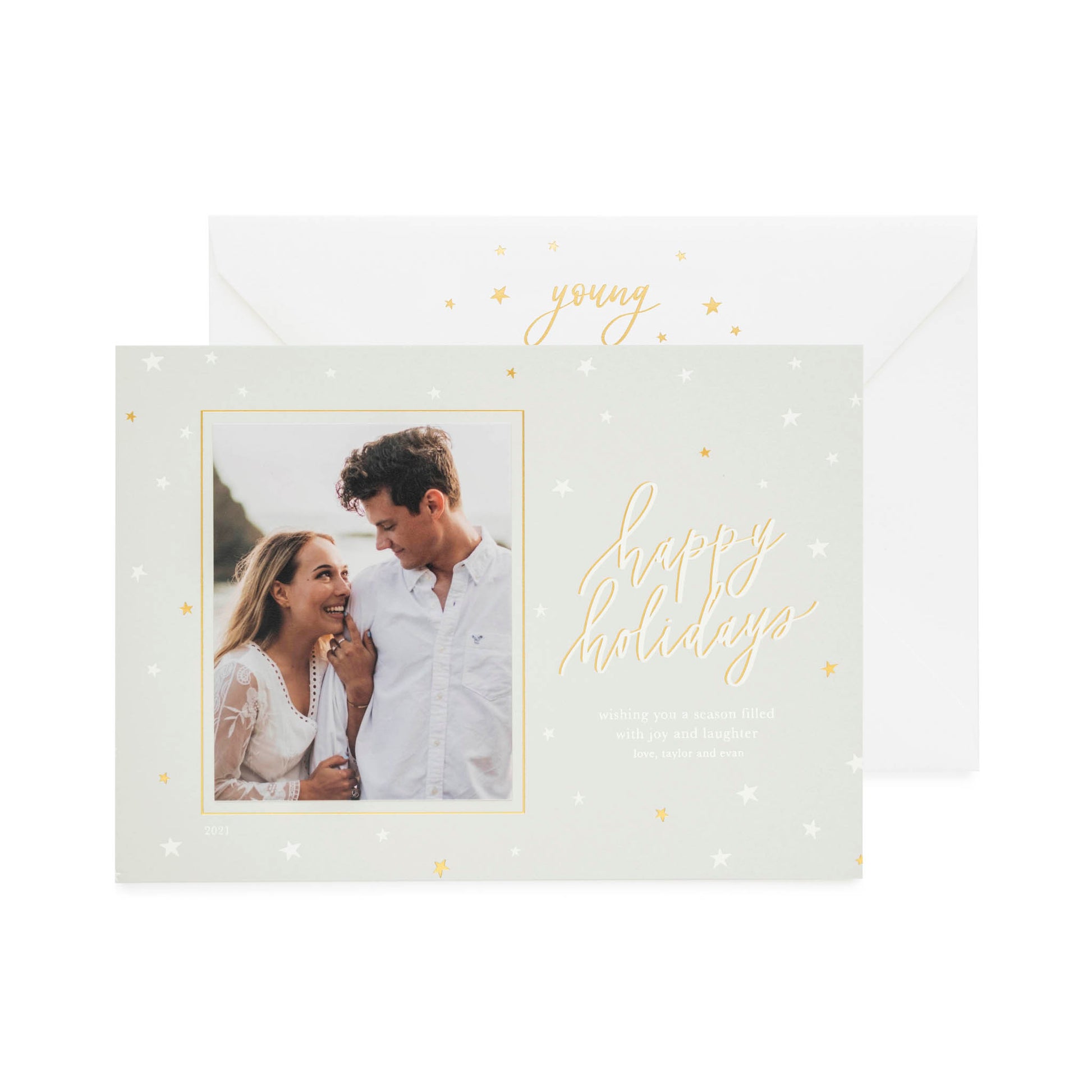 An antique grey custom holiday photo card featuring a picture of a couple with a star decoration pattern, with the text 'Happy Holidays' and a seasonal greeting in gold and white foil paired with a white envelope