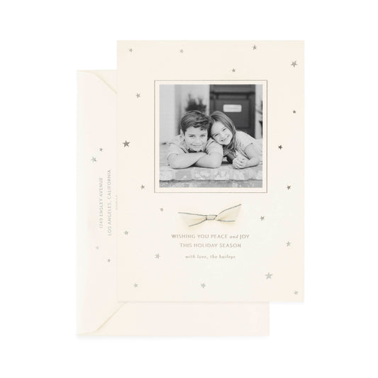 Cream custom holiday photo card with black and white photo of two kids with a cream and silver ribbon and silver printed 'wishing you peace and joy this holiday season'