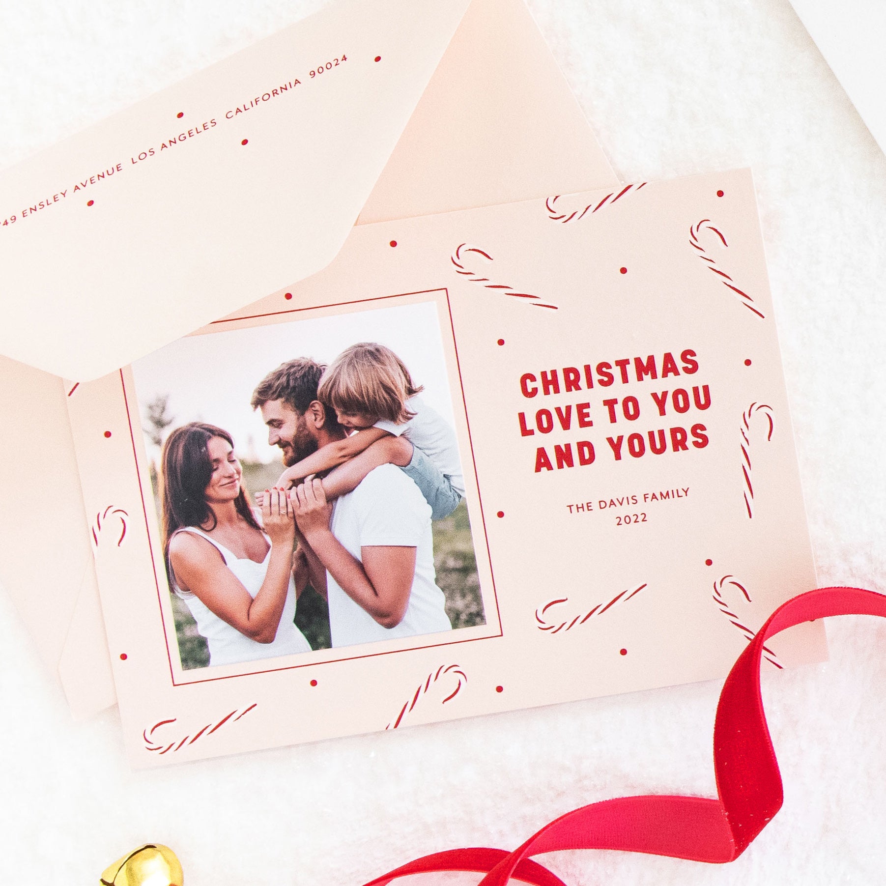 Pink custom holiday photo card printed with white and red candy cane pattern and  'christmas love to you and yours' with a photo of a family with a little boy