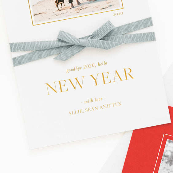 Close up of custom holiday photo card with blue ribbon tied around it in a bow with 'goodbye 2020, hello new year' in gold foil