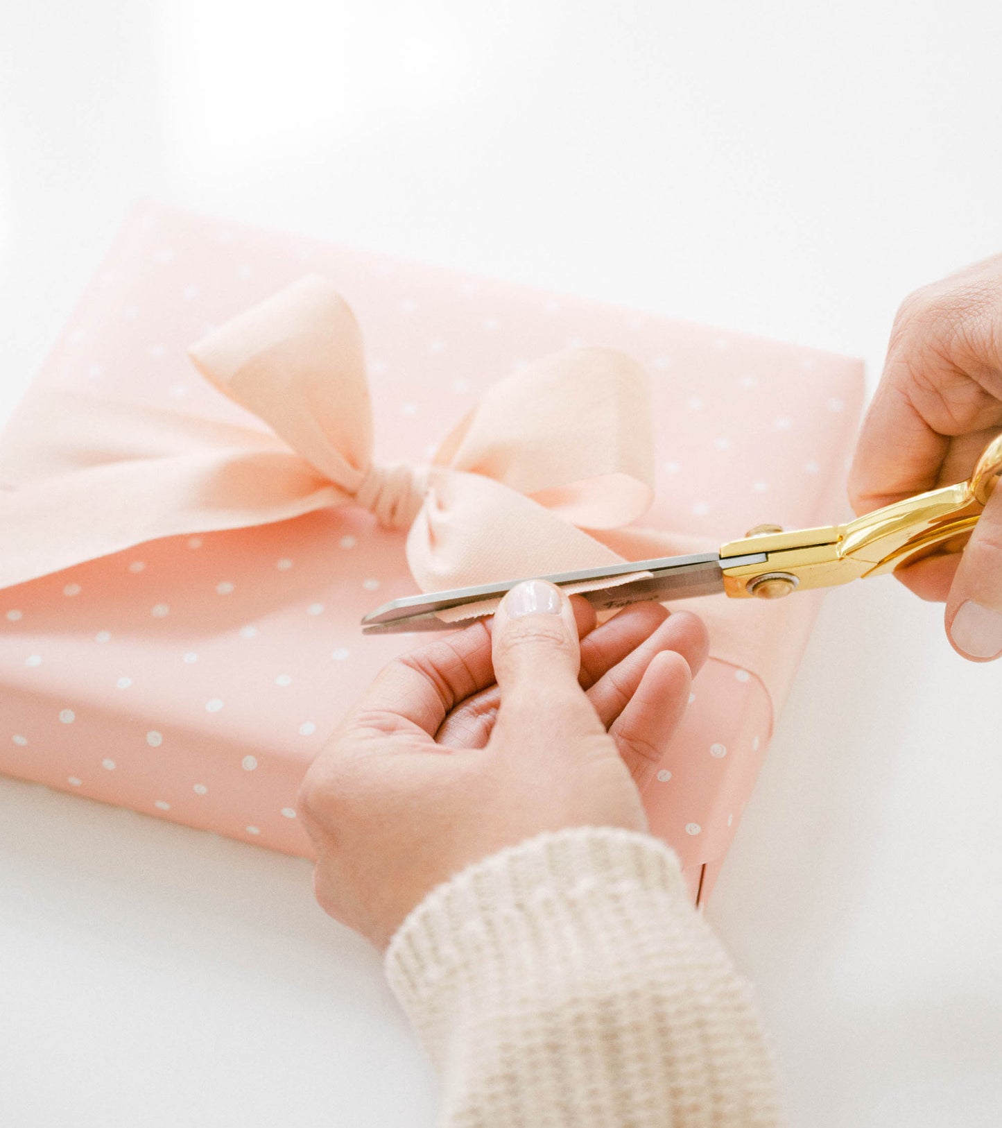 person trimming pale pink bow on rose dot wrapped gift