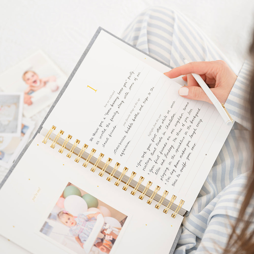 birthday book open to first birthday with a photo of little girl underneath "you're one" and then written prompts for "how we celebrated," "your favorite things at this age," and "highlights from this year"