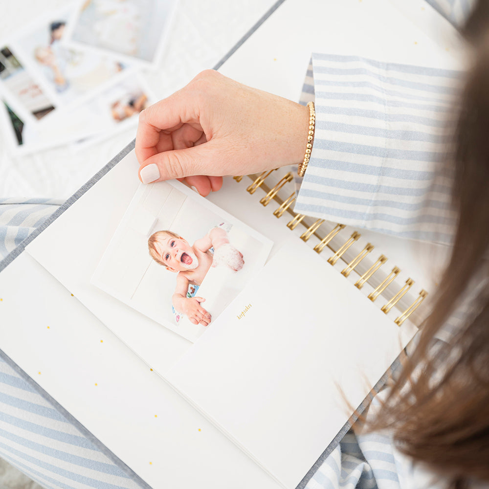 Open birthday book page in hand with hand pulling a photo of a little girl in bath out of "keepsakes" pocket