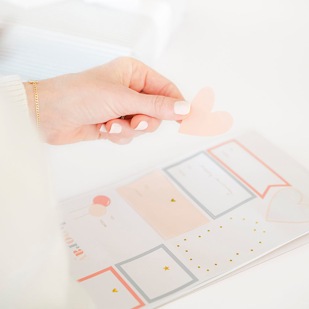 Person picking up one of the stickers from the birthday sticker sheet in colorful pattern of pinks, blues, whites, and golds