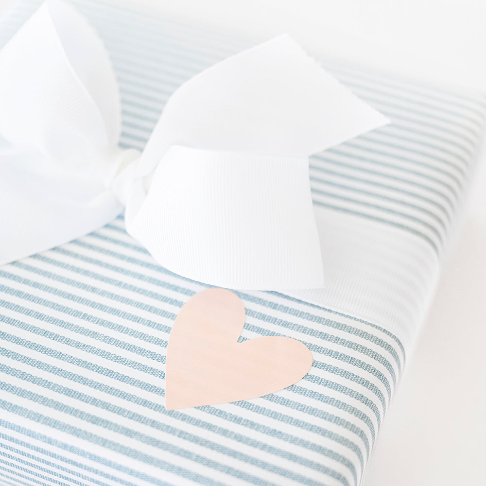Close up of a blue and white striped wrapped gift with a white bow and a pink heart sticker