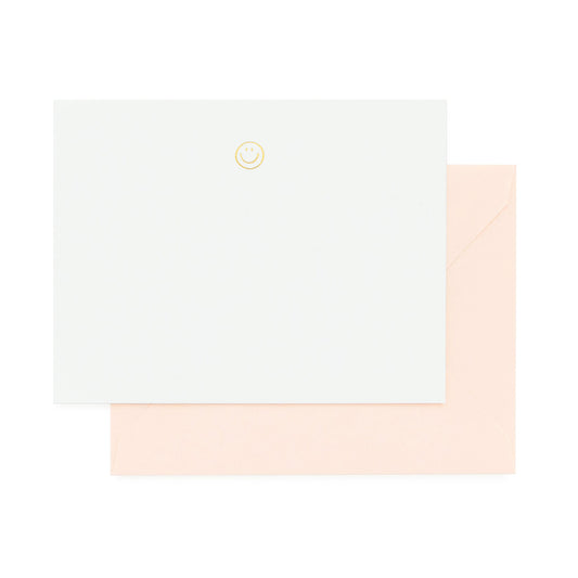 A set of note cards with a gold smiley design on the front, accompanied by a pink envelope.