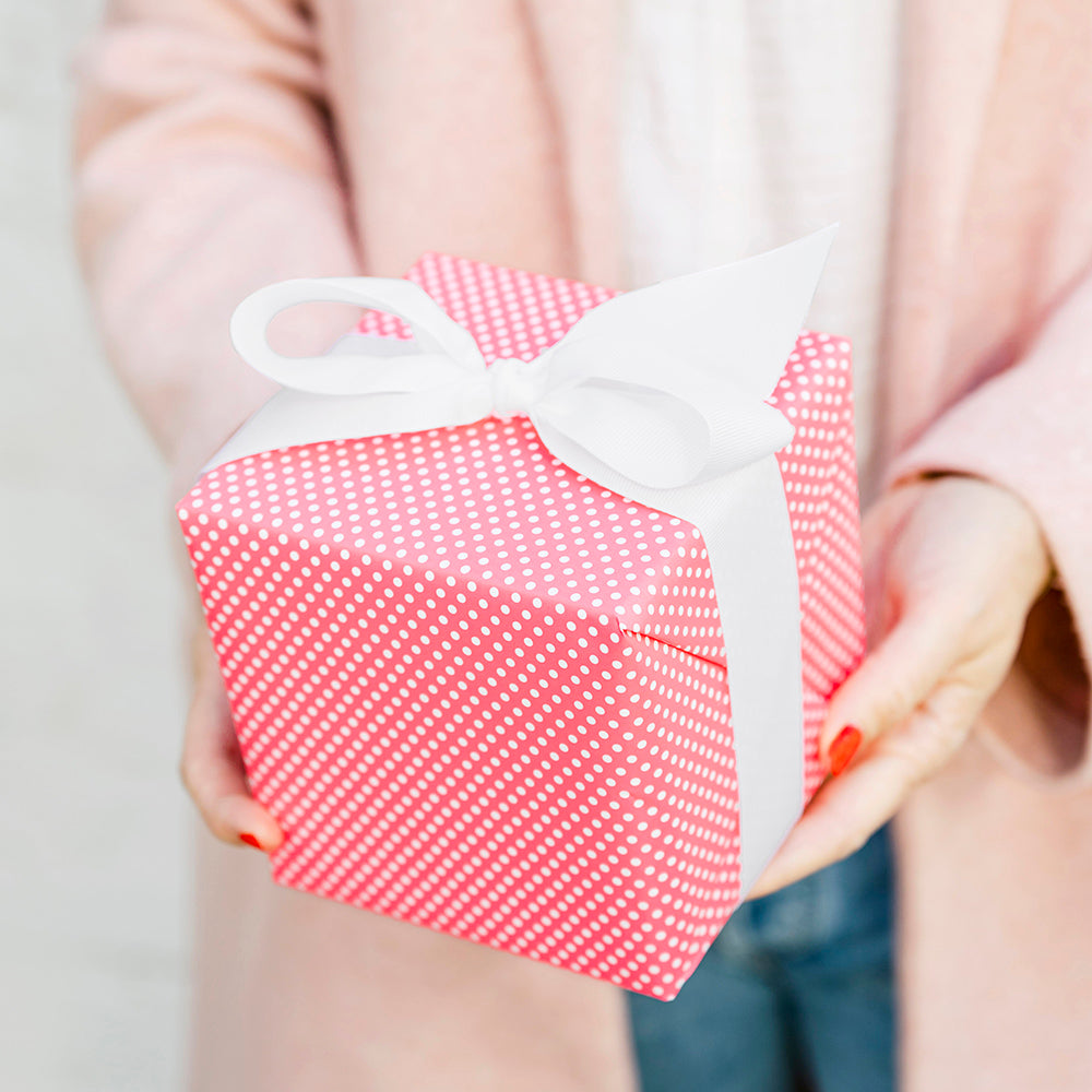 neon and white dot wrapped gift in hands with a big white grosgrain bow