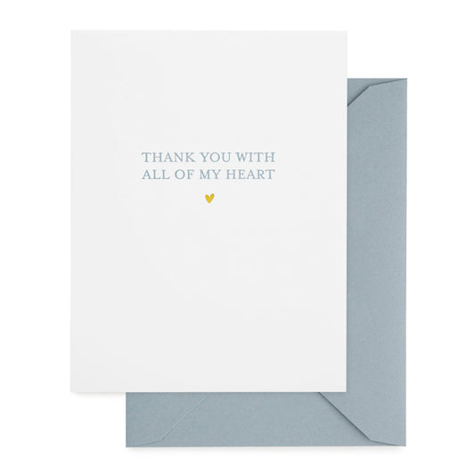 A white greeting card with the text 'THANK YOU WITH ALL OF MY HEART' printed on it in blue ink and gold foil, accompanied by a blue envelope.