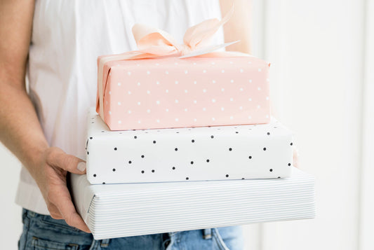 Stack of wrapped gifts in hand in pink dot, black dot, and blue striped