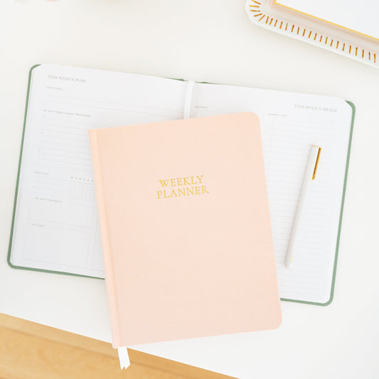 Open undated planner on desk with a pink weekly planner on top