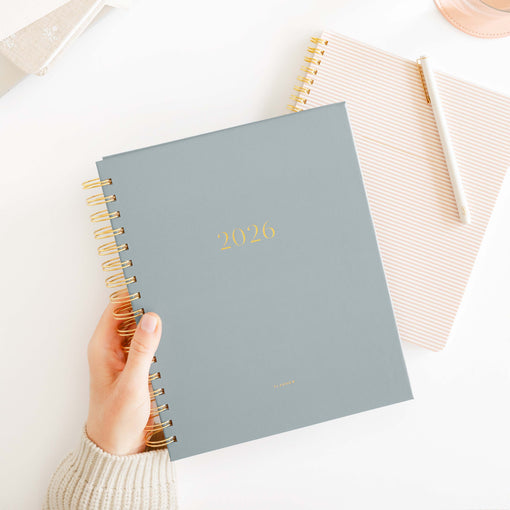 Hand holding a spiral-bound planner with '2026' printed on it against a light background.