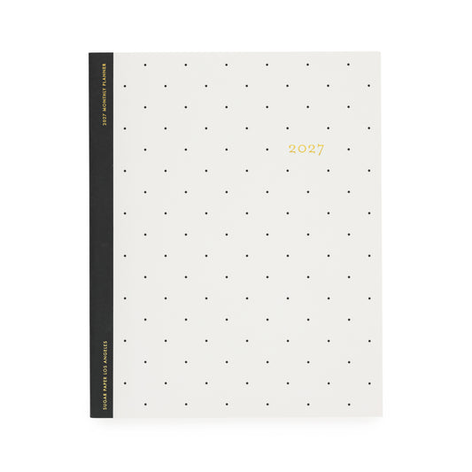 A minimalist 2027 monthly planner with a cream-colored cover decorated with a grid of small black dots and gold foil text with '2027' with a black tape binding