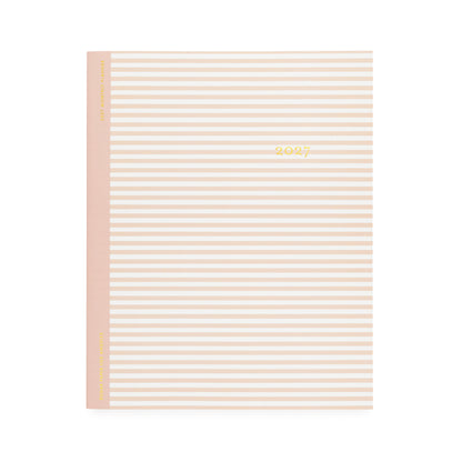 A flat monthly planner with a white and blush pink stripe pattern with '2027' stamped on cover in gold foil with a rose pink tape binding