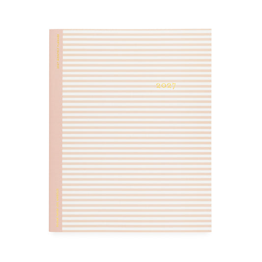 A flat monthly planner with a white and blush pink stripe pattern with '2027' stamped on cover in gold foil with a rose pink tape binding
