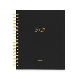 A black 2027 spiral-bound planner with gold foil lettering and a gold wire binding